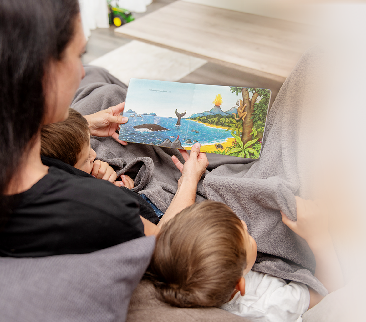 Mama ließt mit zwei Kindern ein Buch. 