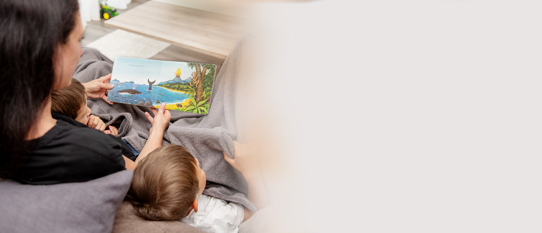 Mama ließt mit zwei Kindern ein Buch. 